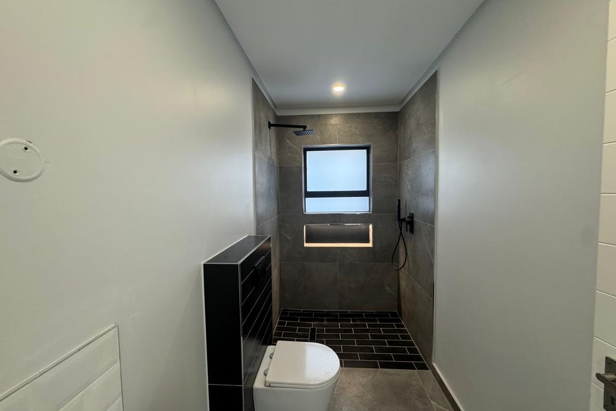 Modern bathroom featuring a wall-mounted toilet, walk-in shower with rain shower head, and contemporary dark tile finishes.