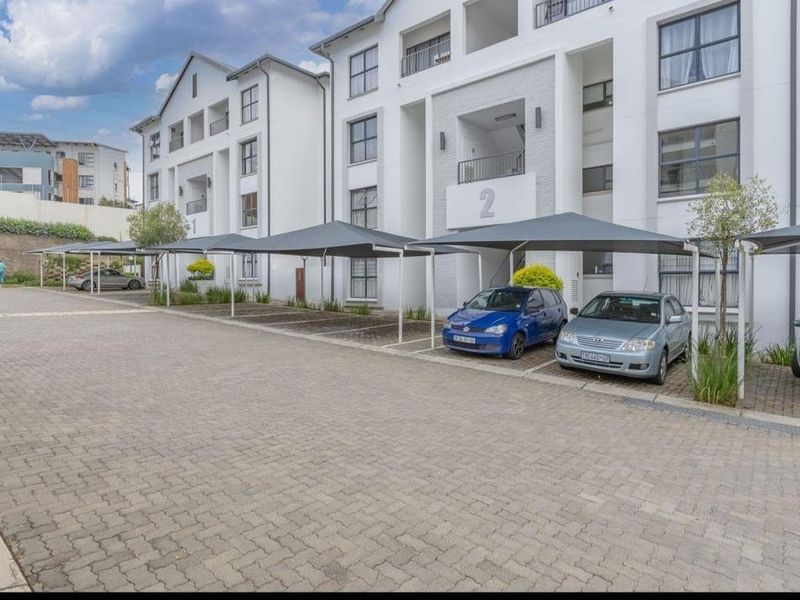 Exterior view of a modern apartment complex featuring paved parking areas with covered bays and multi-story residential units.