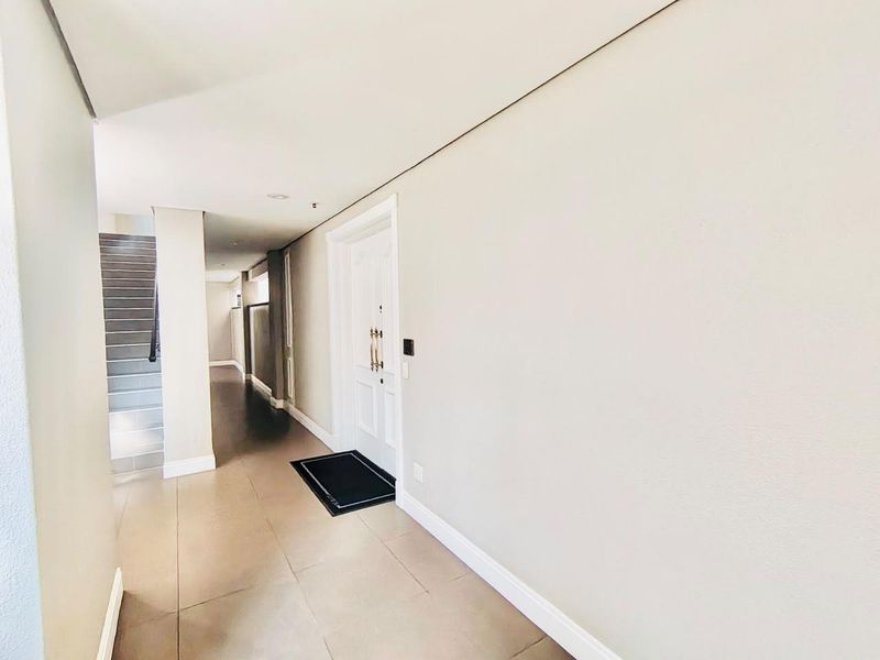 A bright and spacious entrance hall featuring neutral tiled flooring, clean white walls, and a staircase leading to the upper level.
