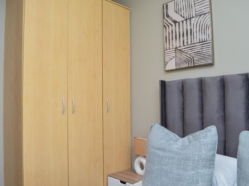 A bedroom featuring a light wood-toned built-in wardrobe with modern silver handles.