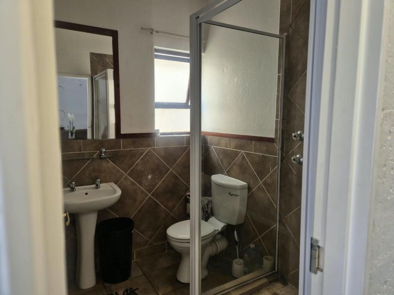 A compact bathroom featuring a pedestal basin, toilet, and a glass-enclosed shower with brown tiled finishes.