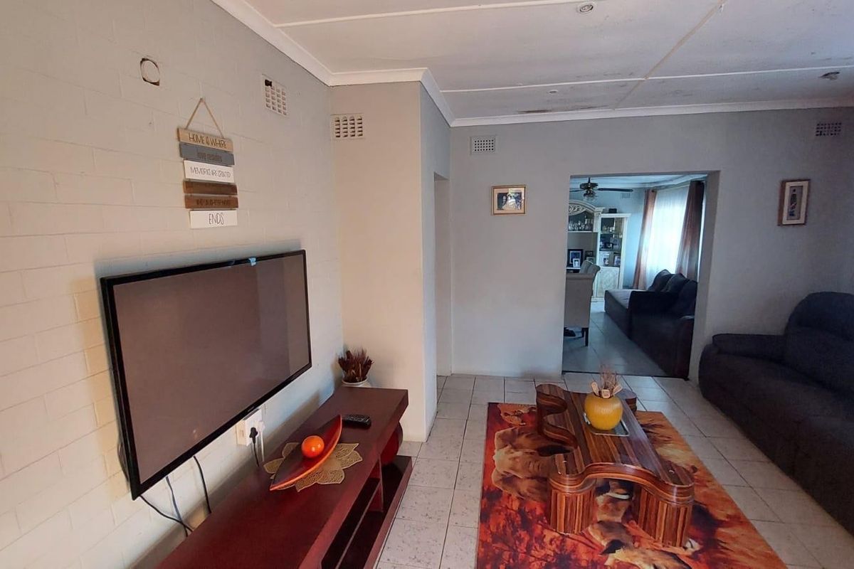 A living room featuring tiled flooring and a painted brick wall, with an open-plan layout leading into an adjacent living space.