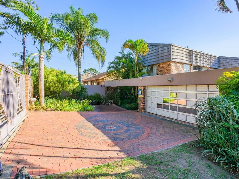 Front exterior view featuring a patterned brick driveway, double garage with glass panel doors, and established garden landscaping.