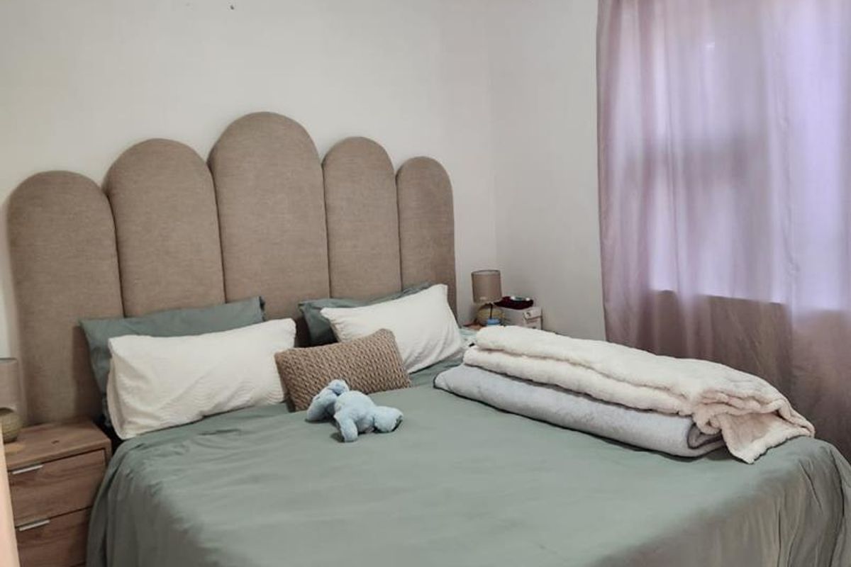 A bedroom featuring laminate flooring and a ceiling light fixture, showing visible signs of ceiling staining and wear.