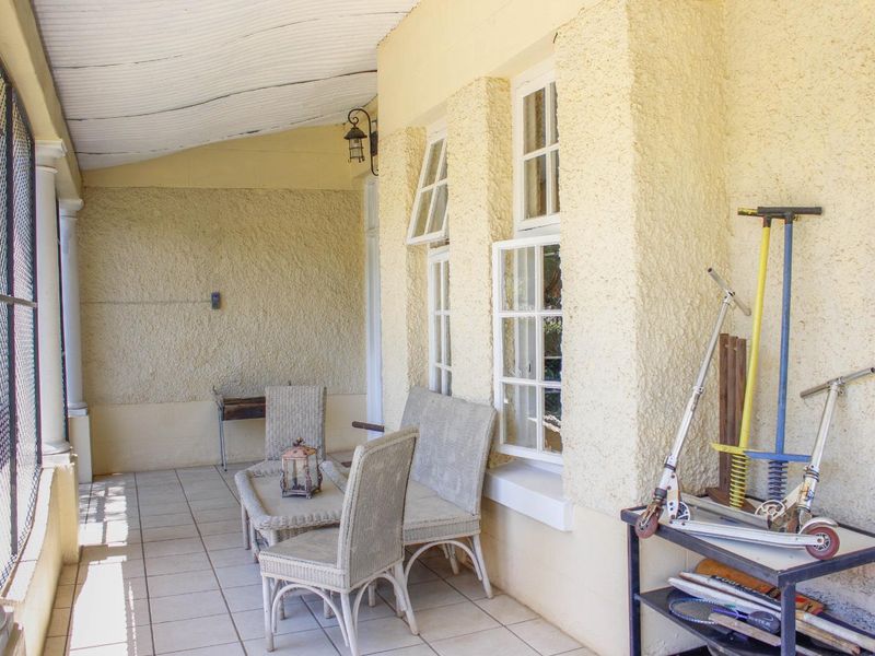 A covered patio area featuring tiled flooring, textured walls, and casement windows, providing a functional outdoor space for relaxation.