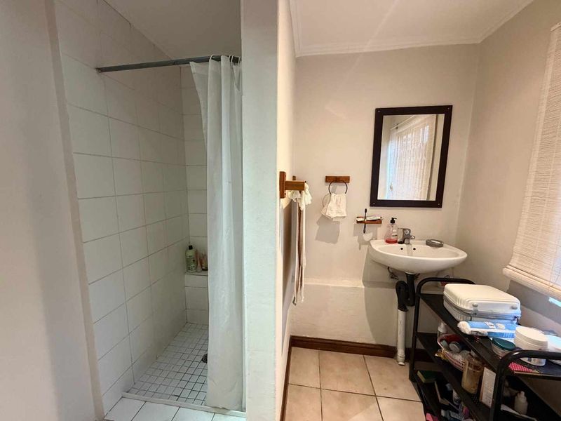 A functional bathroom featuring a tiled shower enclosure, pedestal sink, and wall mirror, currently presenting with dated finishes and exposed plumbing.