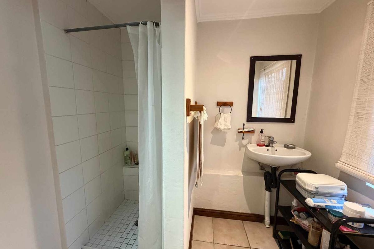 A functional bathroom featuring a tiled shower enclosure, pedestal sink, and wall mirror, currently presenting with dated finishes and exposed plumbing.