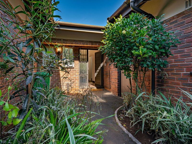 A welcoming front entrance featuring a brick facade, paved walkway, and secure gated entry, surrounded by established garden landscaping.