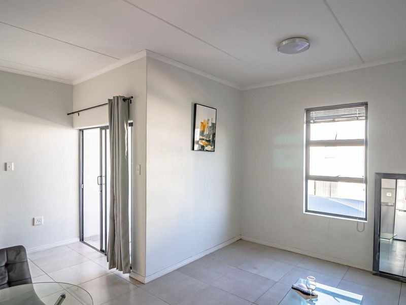 A bright, open-plan living area featuring neutral tiled flooring, a sliding glass door leading to an outdoor space, and large windows for natural light.
