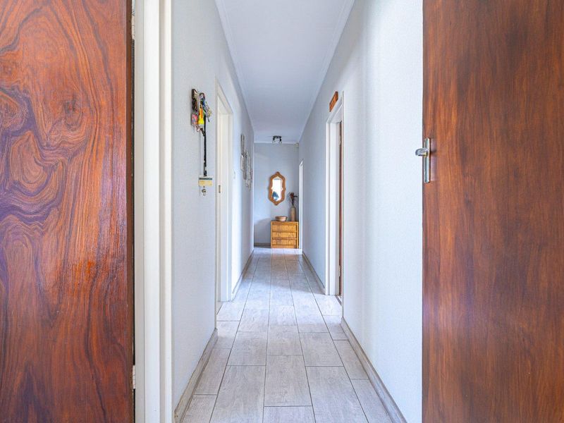 A clean and well-maintained hallway featuring light-toned tiled flooring and classic wooden doors leading to adjacent rooms.