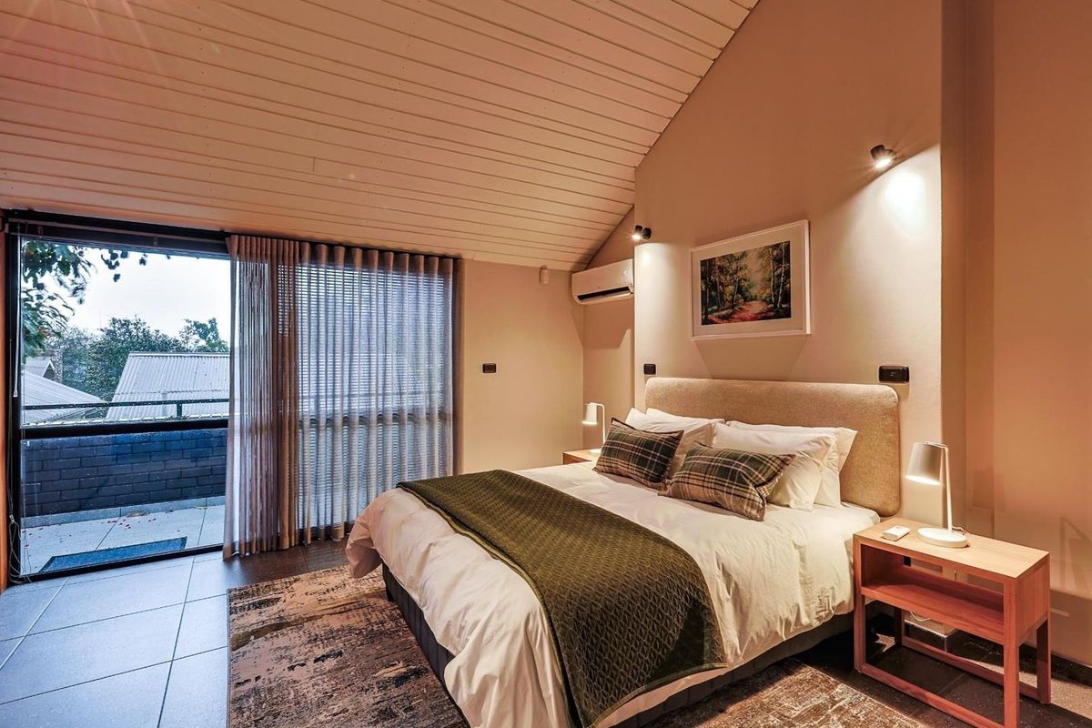 A well-appointed bedroom featuring a vaulted timber ceiling, split-system air conditioning, and large sliding glass doors opening onto a private balcony.
