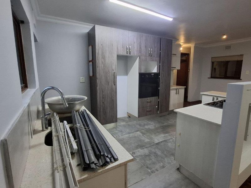 Modern kitchen featuring grey wood-grain cabinetry, stone countertops, built-in oven, and hob, with tiled flooring and a functional layout.