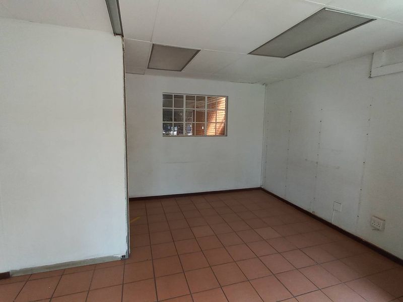 An empty office space featuring tiled flooring, a drop ceiling with recessed lighting, and a small window looking out to an exterior brick wall.