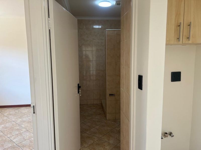 A functional bathroom featuring tiled walls and flooring with a built-in shower enclosure, adjacent to a tiled living area.
