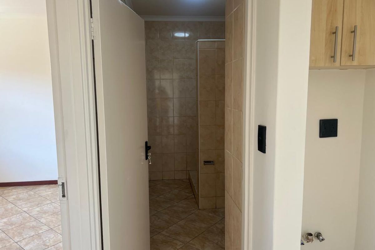A functional bathroom featuring tiled walls and flooring with a built-in shower enclosure, adjacent to a tiled living area.