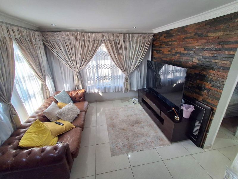 A comfortable living room featuring a textured stone cladding feature wall, neutral tiled flooring, and large windows with security gates.