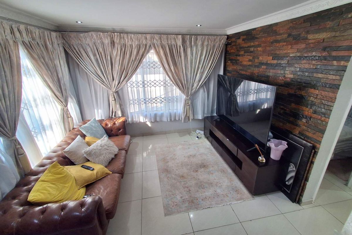 A comfortable living room featuring a textured stone cladding feature wall, neutral tiled flooring, and large windows with security gates.