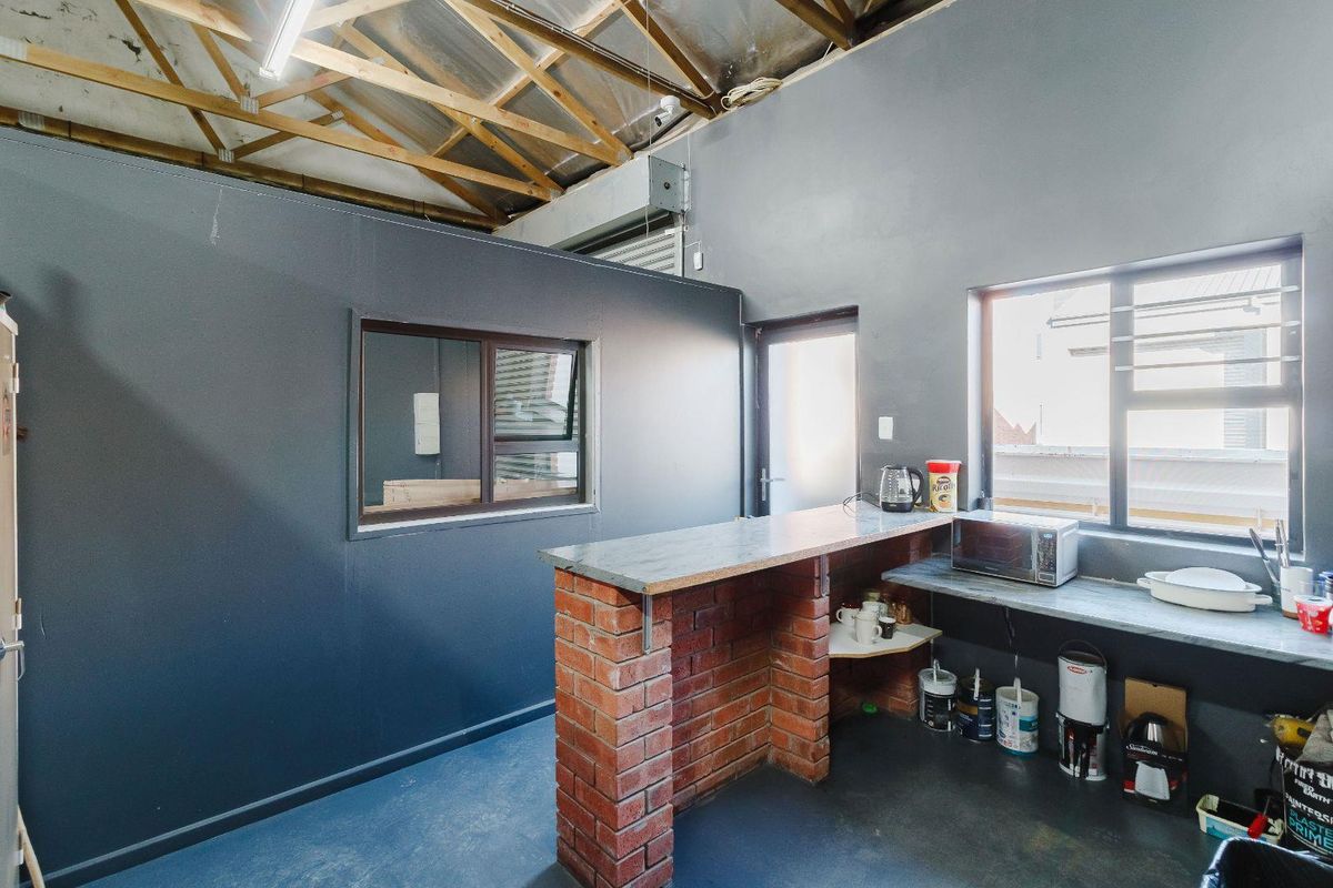 A functional kitchen area featuring exposed timber roof trusses, a brick breakfast bar with stone countertop, and painted concrete flooring.
