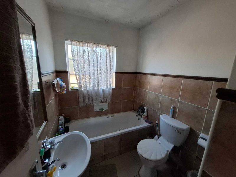 A dated bathroom featuring a bathtub, pedestal basin, and toilet with tiled walls and flooring, showing signs of ceiling wear and maintenance needs.