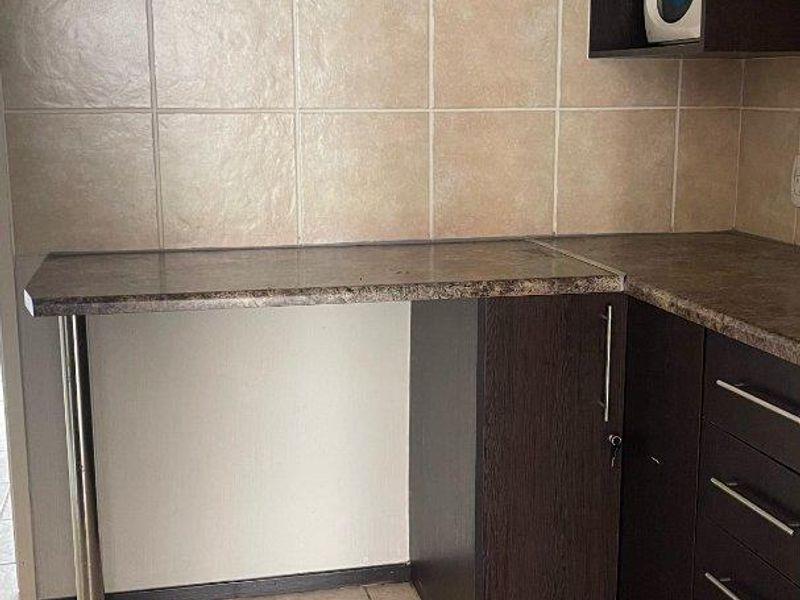 A functional kitchen corner featuring dark wood cabinetry, laminate countertops, and neutral ceramic tile flooring and backsplash.
