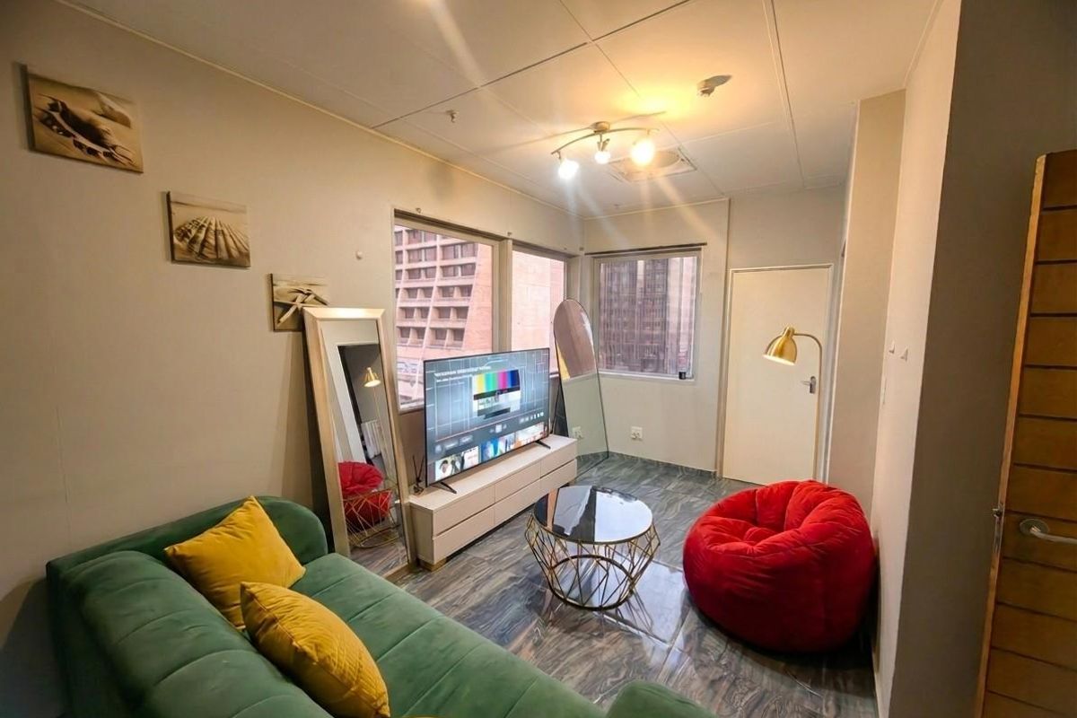 A compact living room featuring tiled flooring, a drop ceiling with integrated lighting, and large windows providing natural light and urban views.