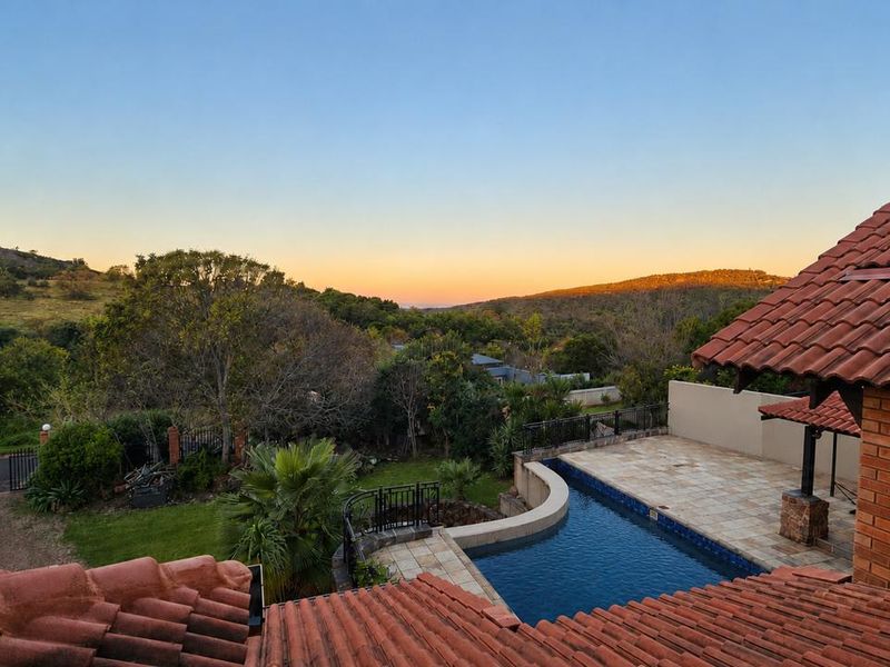 Elevated view overlooking a private swimming pool, paved patio area, and lush landscaped garden with scenic rolling hills in the background.