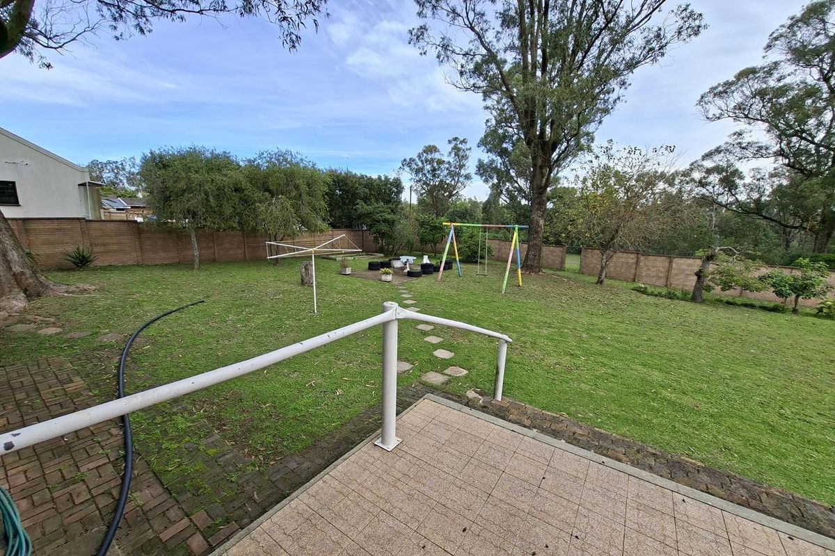 Spacious rear garden featuring a paved patio area, metal handrail, and established lawn enclosed by brick boundary walls.