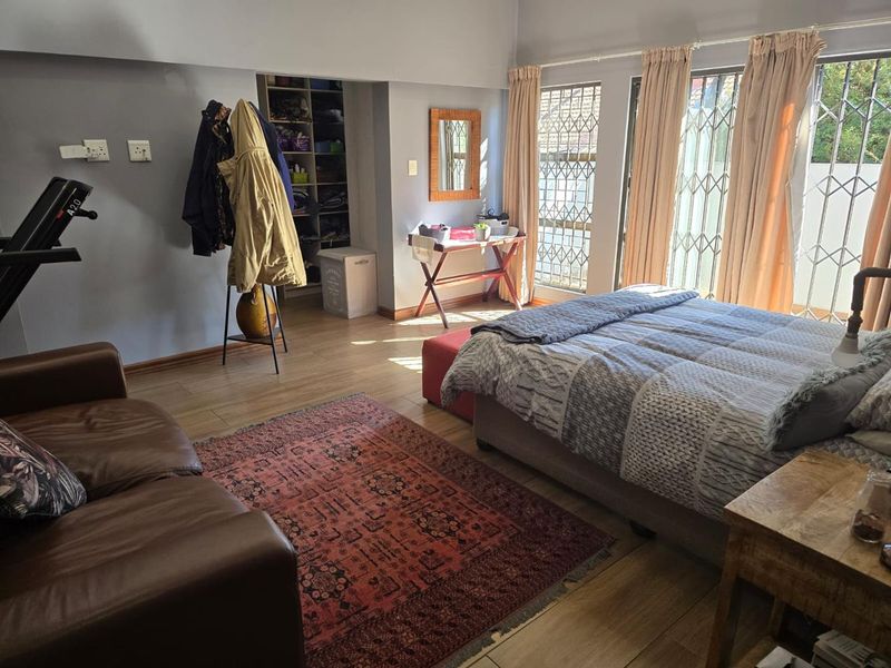 Spacious bedroom featuring laminate flooring, built-in shelving, and sliding glass doors with security gates, offering natural light and direct access to the exterior.