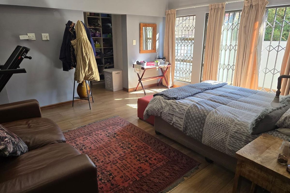 Spacious bedroom featuring laminate flooring, built-in shelving, and sliding glass doors with security gates, offering natural light and direct access to the exterior.