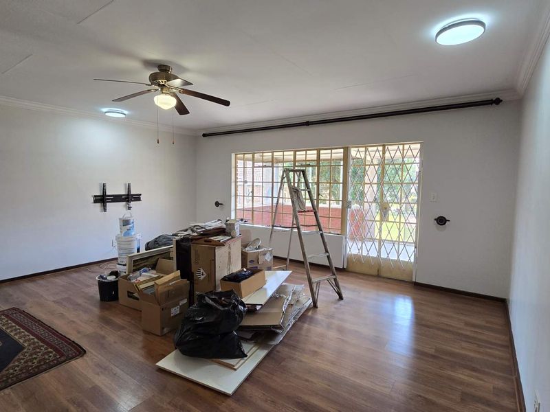 Spacious living area featuring laminate flooring, a ceiling fan, and a sliding glass door with a security gate leading to the exterior.