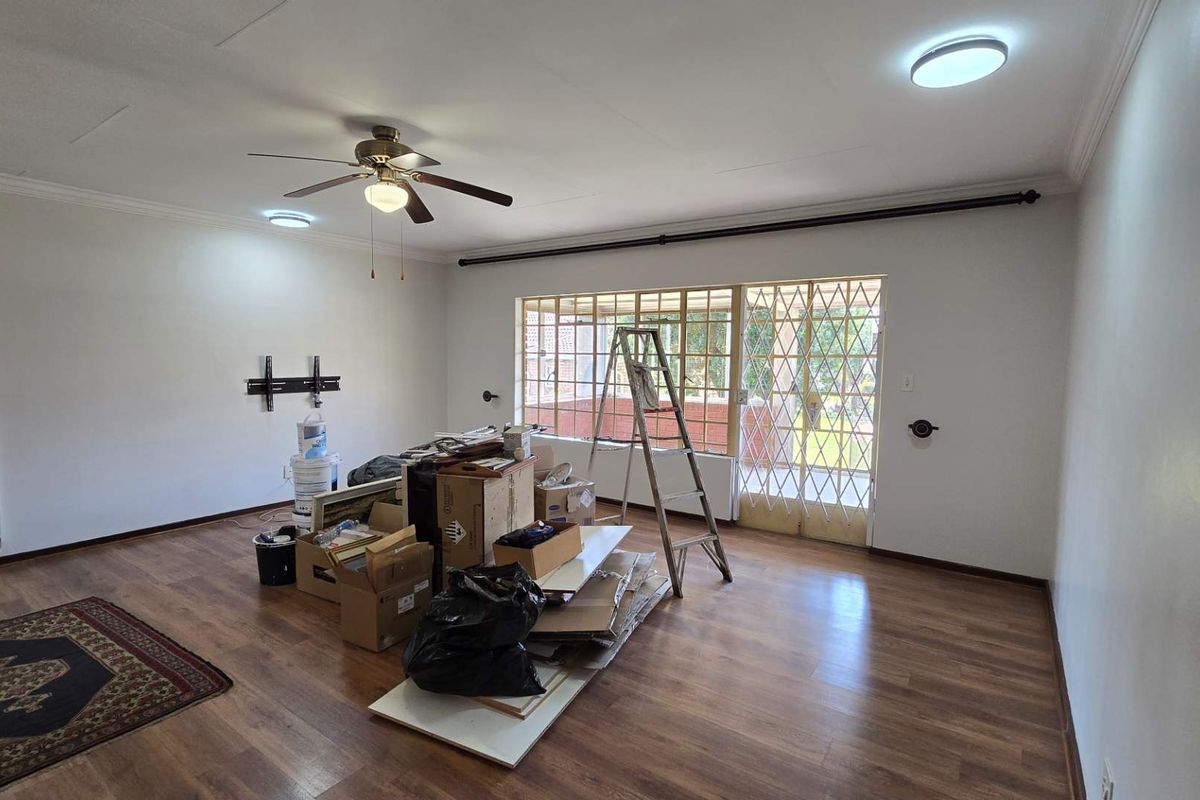 Spacious living area featuring laminate flooring, a ceiling fan, and a sliding glass door with a security gate leading to the exterior.