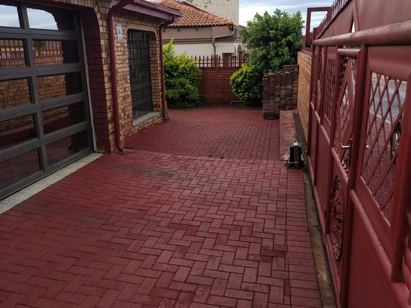 Front exterior view featuring a paved driveway, secure metal gate, and brick facade with a modern sectional garage door.