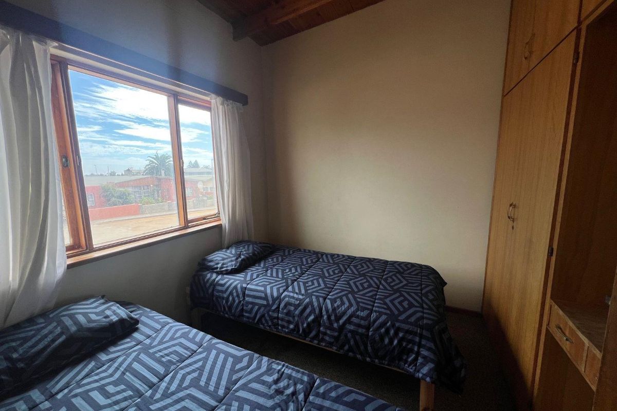 A bedroom featuring built-in wooden cupboards, a timber-beamed ceiling, and a large window providing natural light.