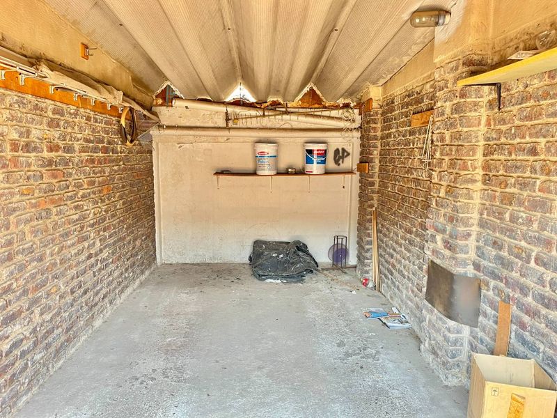 A basic, unfinished garage space featuring exposed brick walls, a corrugated roof, and a concrete floor, offering potential for storage or workshop conversion.