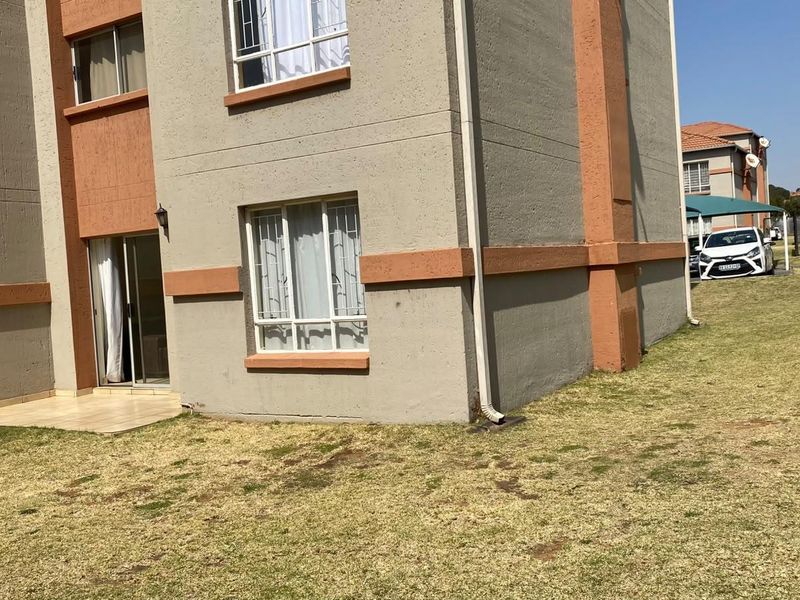 Rear view of the apartment building showing a small tiled patio area, sliding door access, and surrounding communal lawn space.