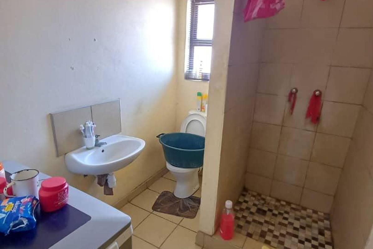 A functional bathroom featuring a wall-mounted basin, toilet, and a tiled shower enclosure with basic finishes.