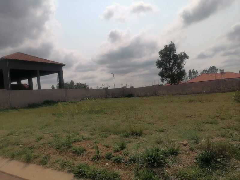 A vacant residential plot featuring a perimeter wall and an adjacent covered structure under a cloudy sky.