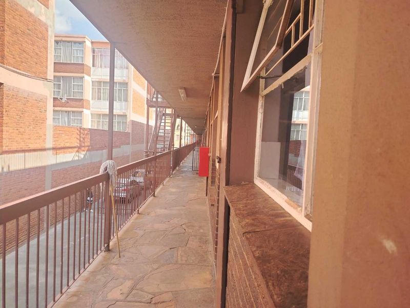 An exterior apartment balcony walkway featuring stone paving, metal railings, and access to adjacent apartment windows.