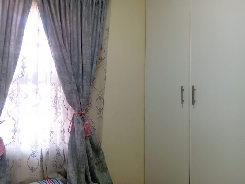 A bedroom interior featuring a built-in wardrobe and a window with decorative curtains.
