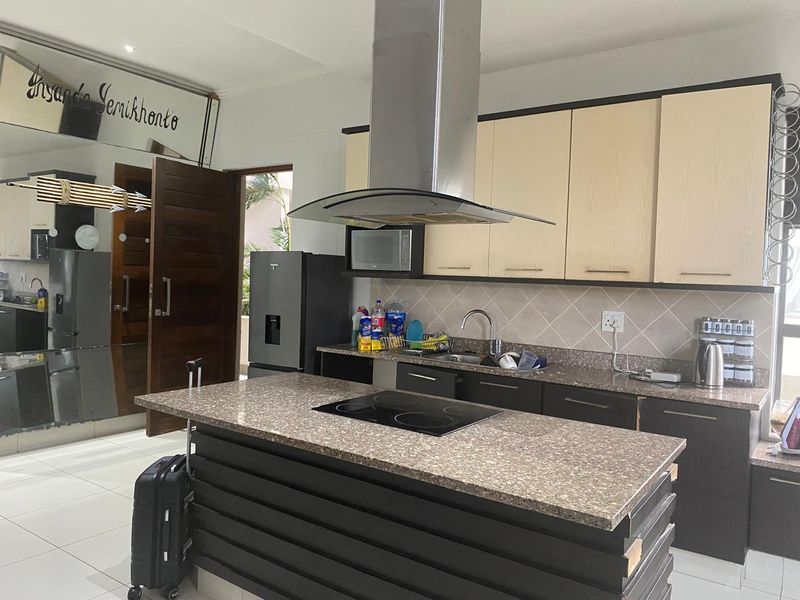 Modern kitchen featuring a central island with a built-in hob, stainless steel extractor fan, stone countertops, and ample built-in cabinetry.