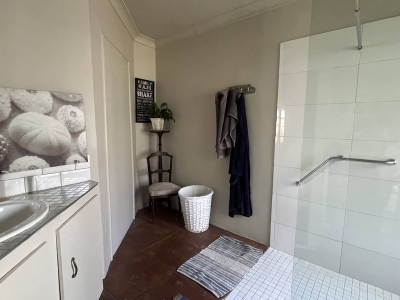 A functional bathroom featuring a vanity with a tiled countertop, a walk-in shower with a glass screen, and a safety grab rail.