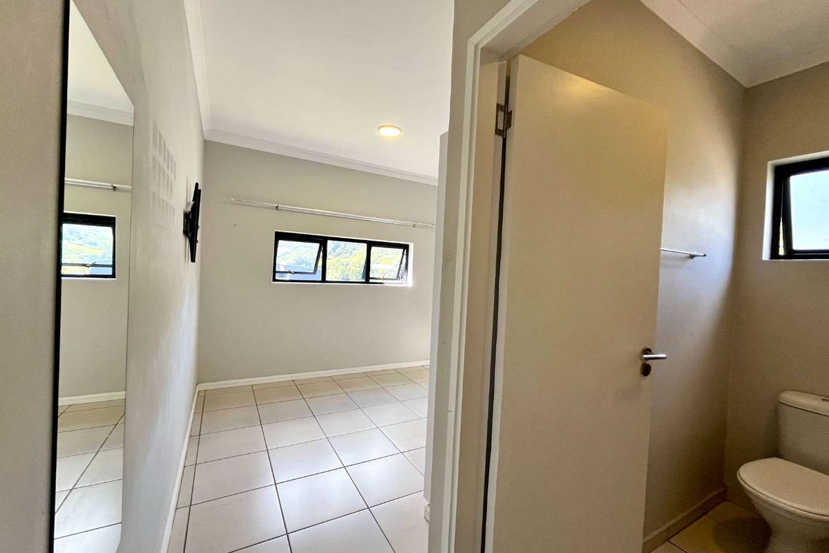 A bright, empty bedroom featuring neutral tiled flooring, recessed lighting, and aluminium-framed windows, with an adjacent bathroom visible through the doorway.