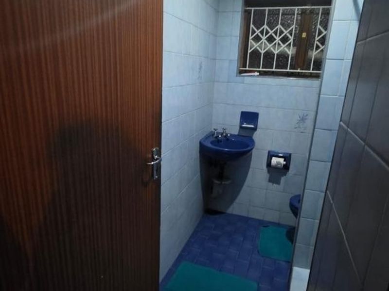 A dated bathroom featuring blue sanitaryware, tiled surfaces, and a security grille on the window, requiring modernization to improve its aesthetic and functionality.