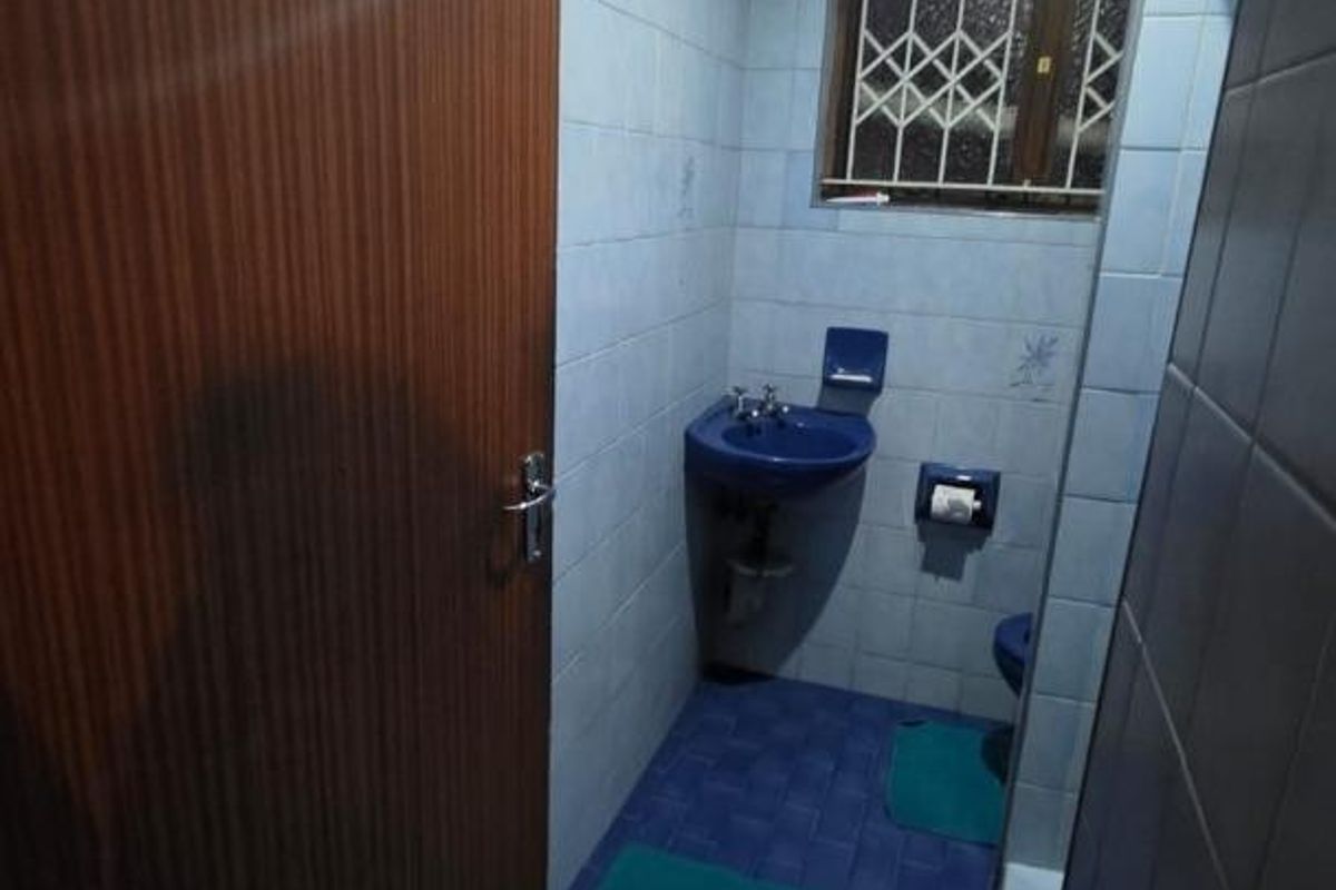 A dated bathroom featuring blue sanitaryware, tiled surfaces, and a security grille on the window, requiring modernization to improve its aesthetic and functionality.