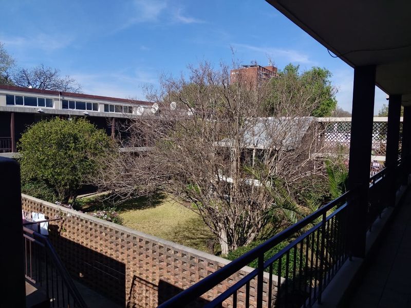 A covered balcony overlooking a communal garden area with established trees and brick boundary walls.