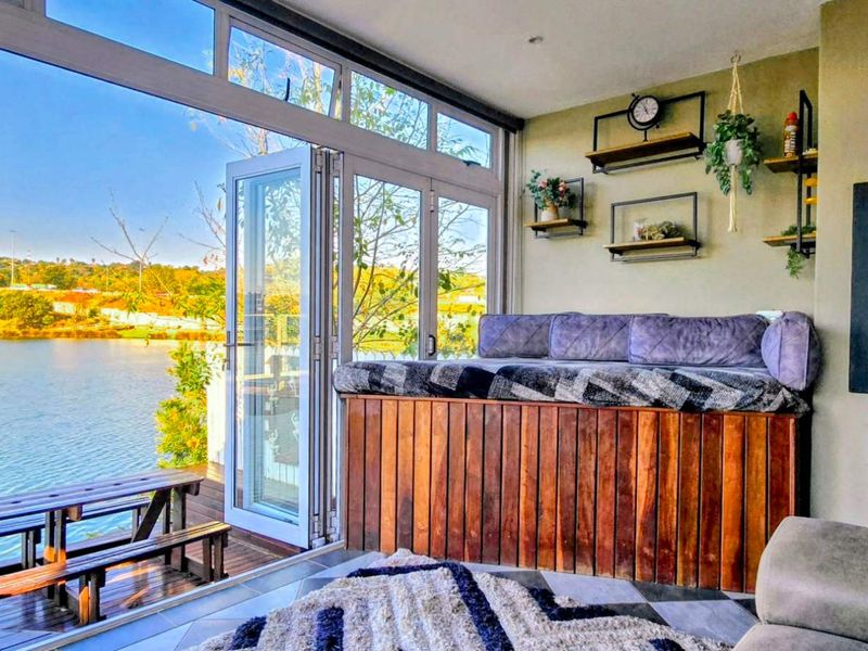 A modern living room featuring a built-in fireplace and expansive bi-fold doors opening onto a wooden deck with scenic waterfront views.