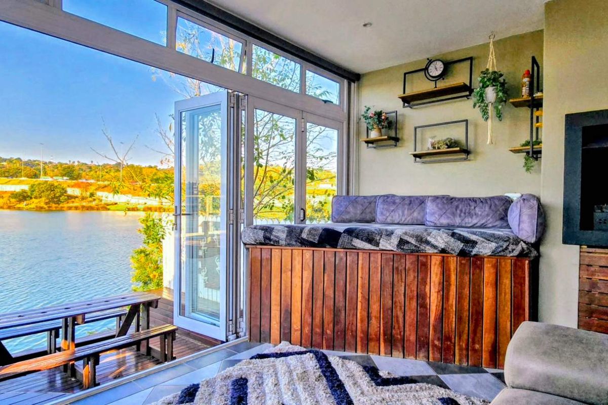 A modern living room featuring a built-in fireplace and expansive bi-fold doors opening onto a wooden deck with scenic waterfront views.