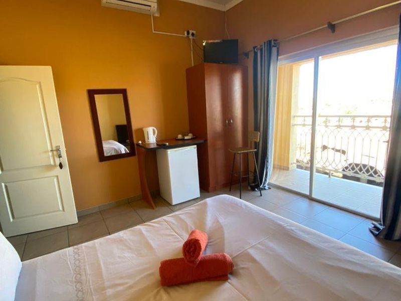 A hotel bedroom featuring tiled flooring, a split-system air conditioner, and sliding glass doors leading to a balcony with a wrought iron railing.
