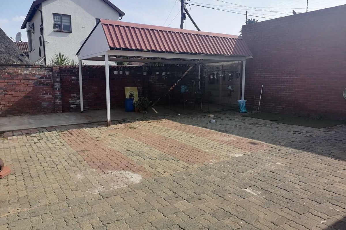 Rear exterior area featuring a paved driveway and a covered carport structure enclosed by brick boundary walls.