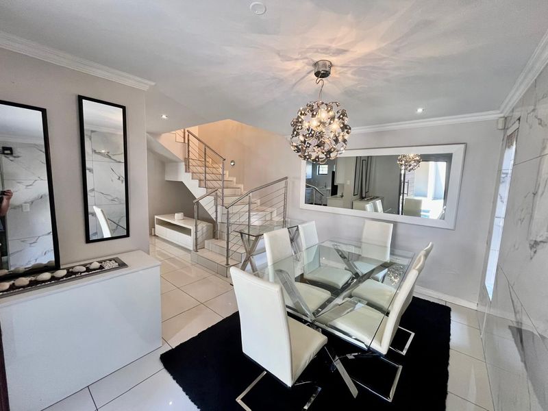 Modern open-plan dining area featuring sleek porcelain floor tiles, a contemporary staircase with stainless steel balustrades, and elegant recessed lighting.
